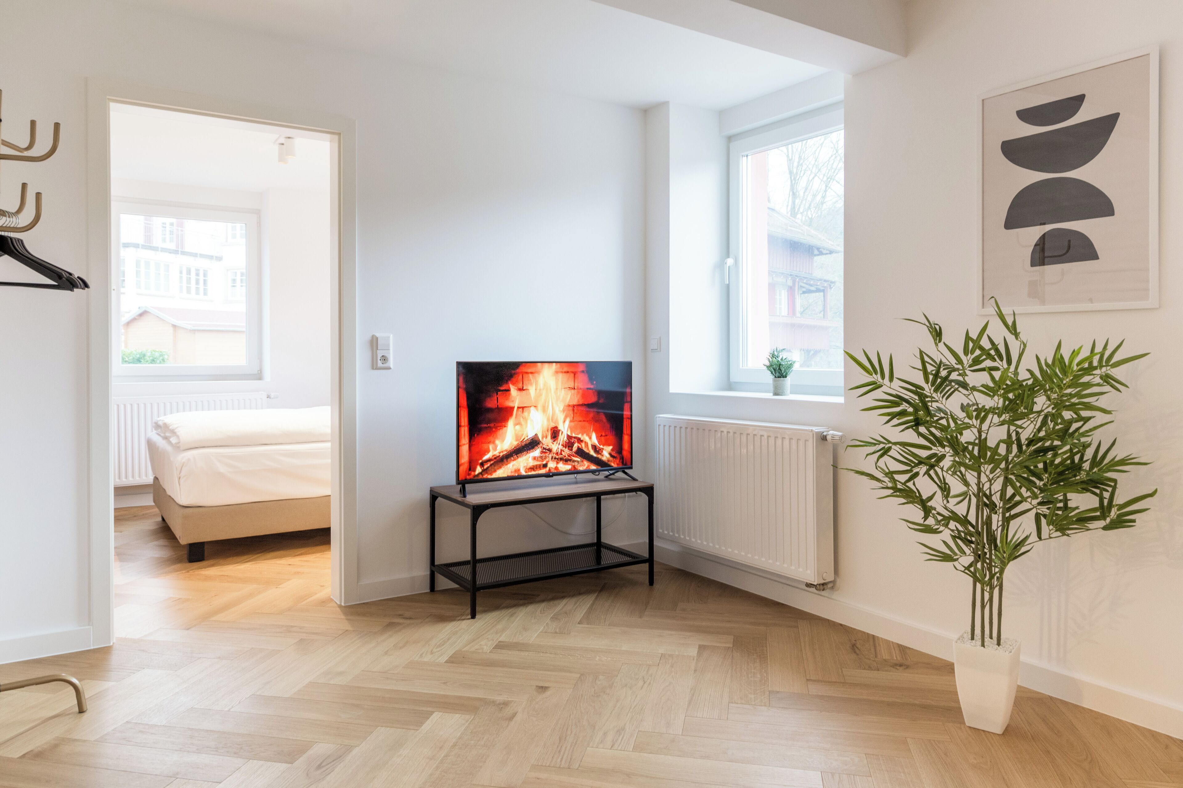Una sala de estar moderna con una televisión mostrando una chimenea, una cama y una planta en maceta.