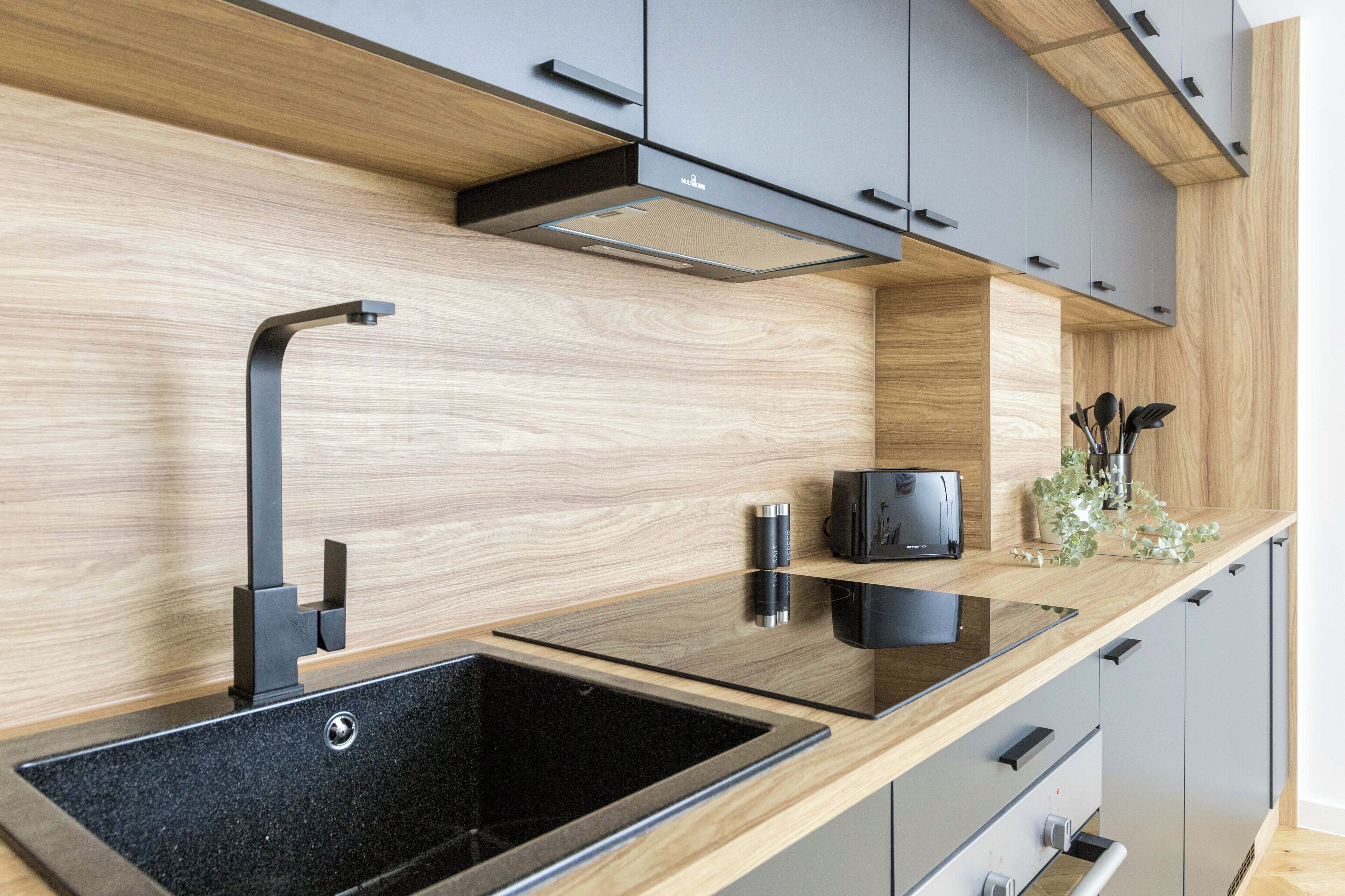 A modern kitchen with a wooden backsplash, a black sink, and grey cabinets.