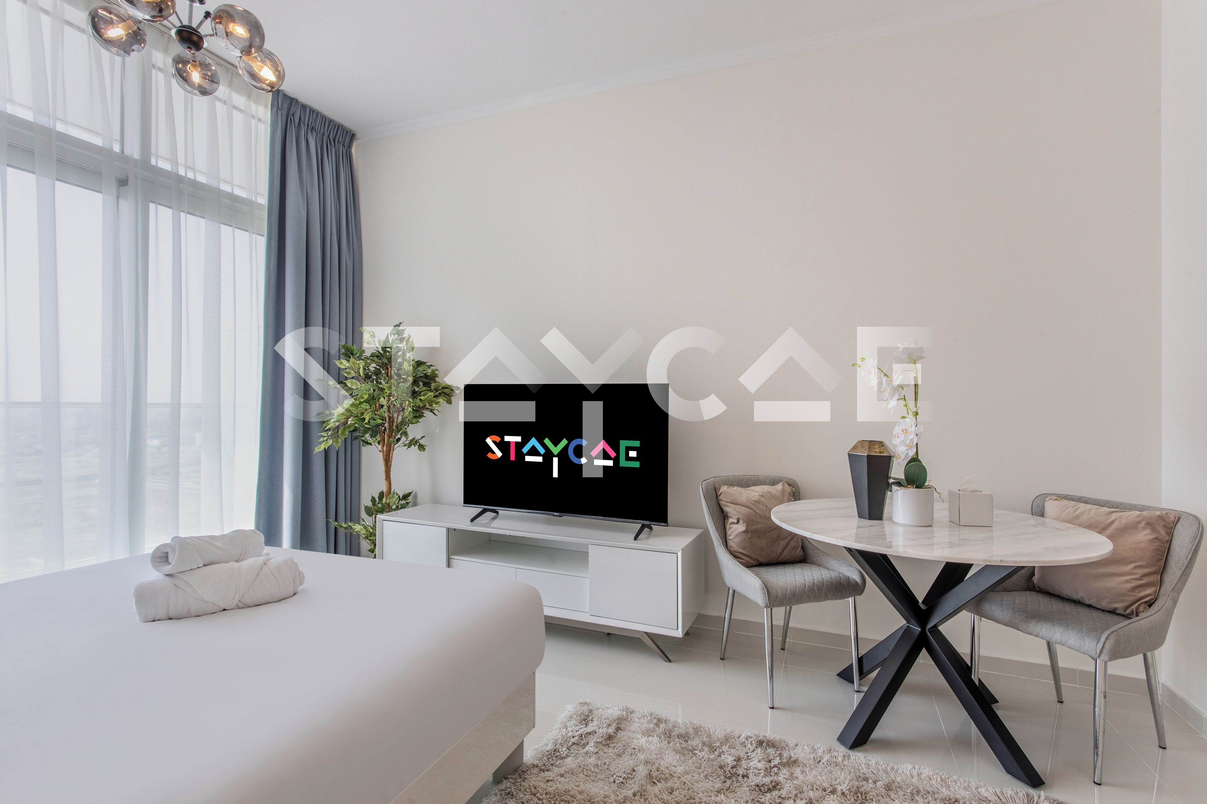 Een moderne hotelkamer met een bed, een televisie, een eettafel en een plant.