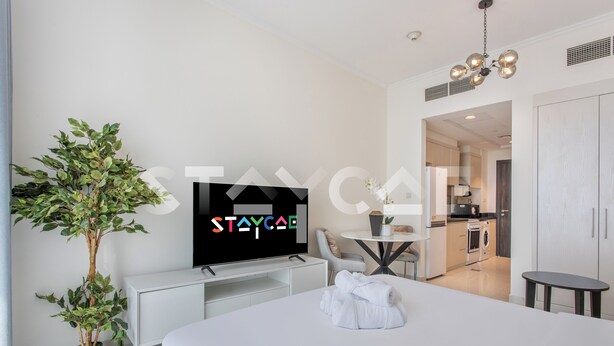 A modern hotel room with a bed, a TV, a potted plant, and a view into the kitchen. - Staycae Holiday Homes - Carson Tower (Dubai)