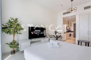 A modern hotel room with a bed, a TV, a potted plant, and a view into the kitchen. - Staycae Holiday Homes - Carson Tower (Dubai)