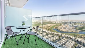 A balcony with two chairs and a small table, overlooking a cityscape with buildings and a river. - Staycae Holiday Homes - Carson Tower (Dubai)