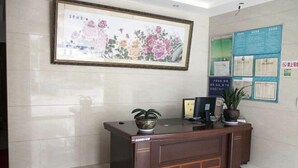 A reception desk with a framed floral artwork above it, a potted plant on the desk, and a bulletin board with various notices to the right. - Jinyuan Hostel (Yueqing)