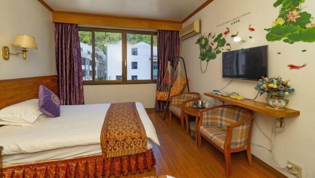 A hotel room with a bed, a desk, a chair, a TV, and a window with curtains. - Jinyuan Hostel (Yueqing)