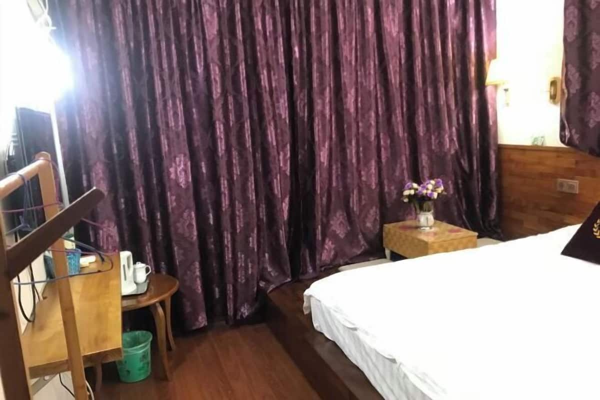A bedroom with a bed, a chair, a small table with a vase of flowers, and a curtain.