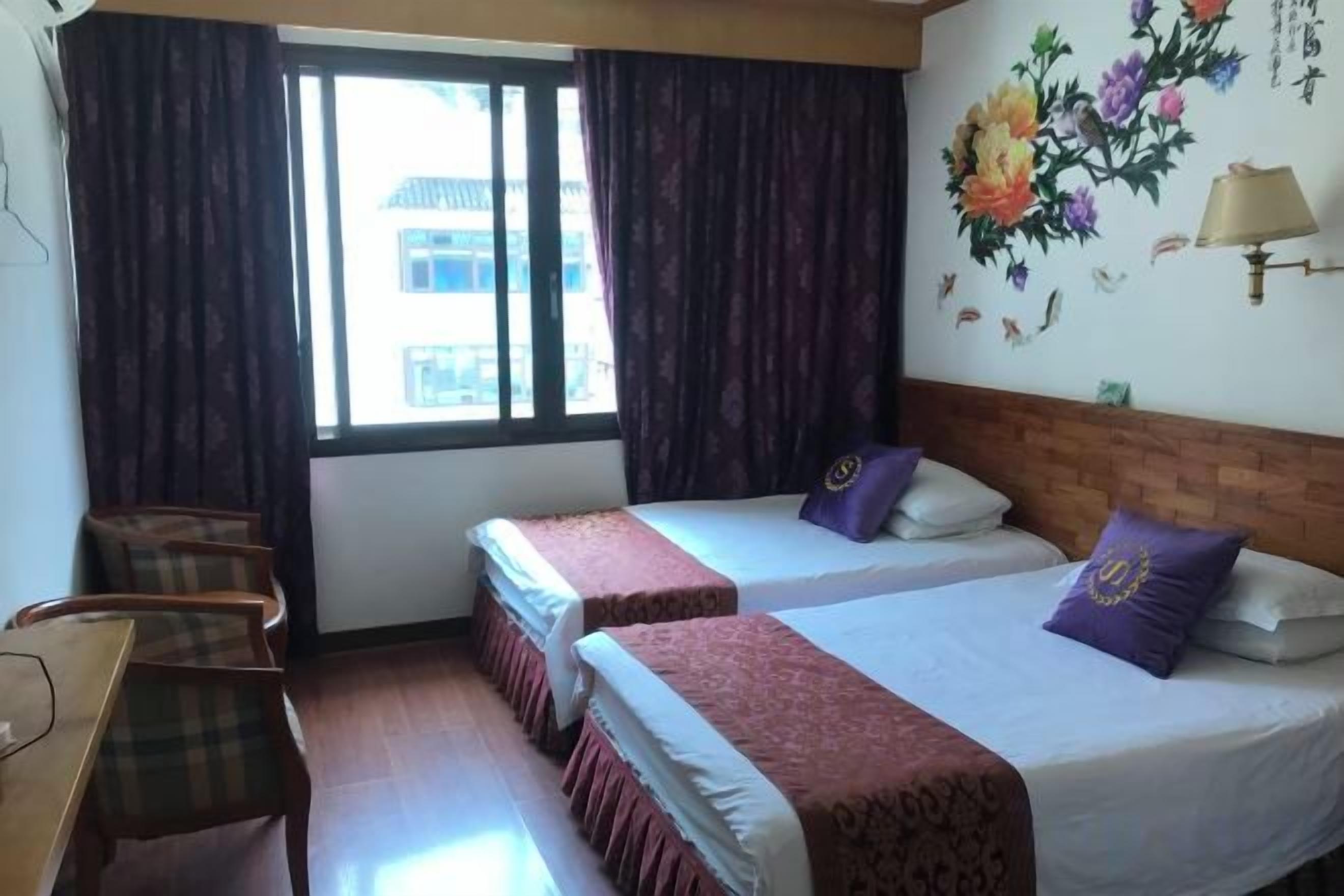 A hotel room with two beds, a desk, and a window with curtains.