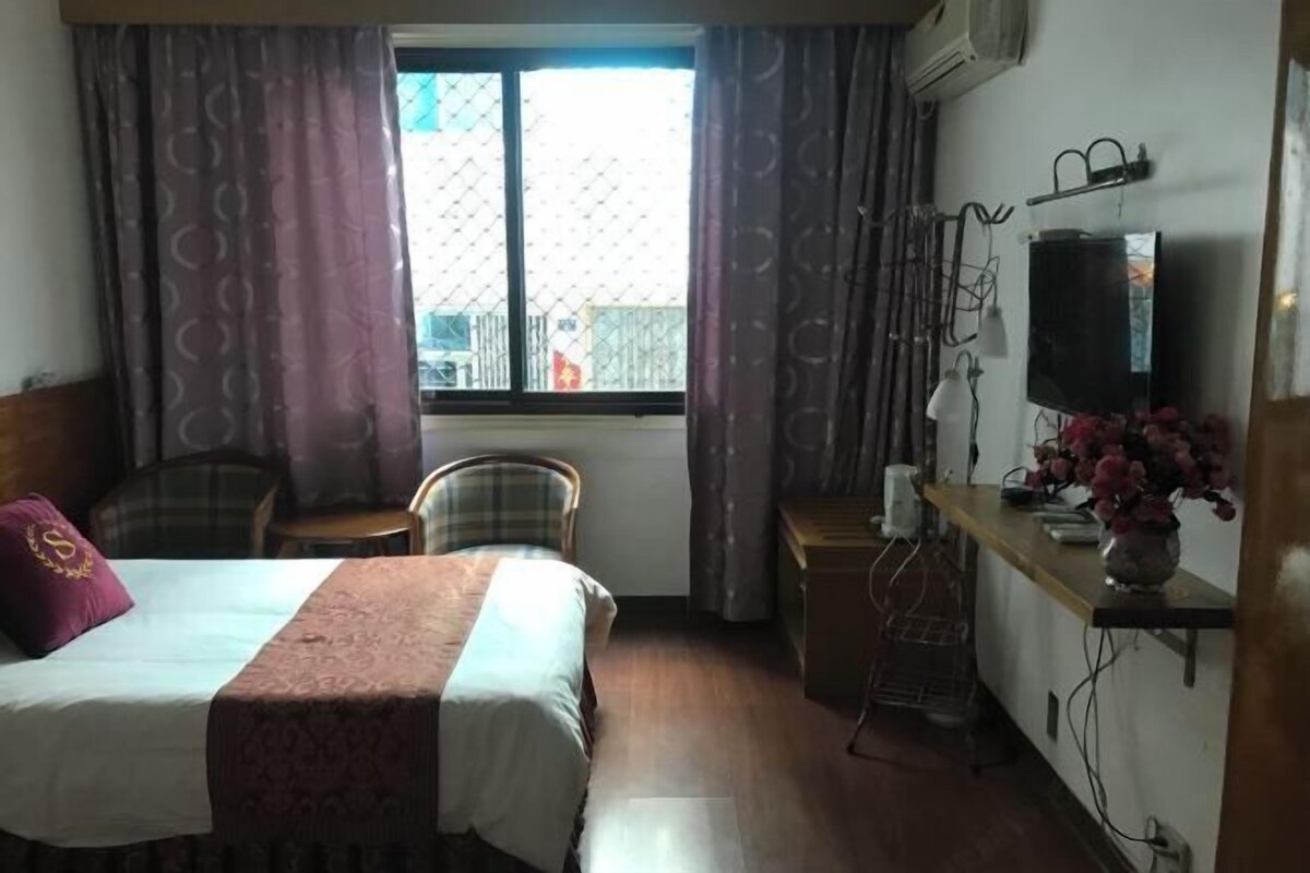 A hotel room with a bed, a desk, a chair, a TV, and a window with curtains.