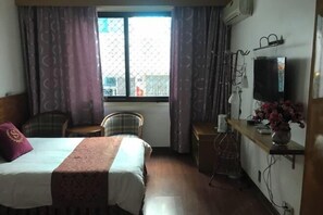 A hotel room with a bed, a desk, a chair, a TV, and a window with curtains. - Jinyuan Hostel (Yueqing)
