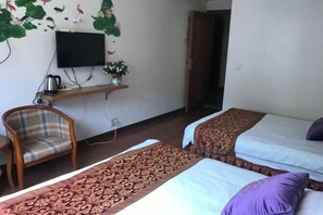A room with two beds, a television mounted on the wall, a wooden chair, and a small table with a kettle and flowers. - Jinyuan Hostel (Yueqing)
