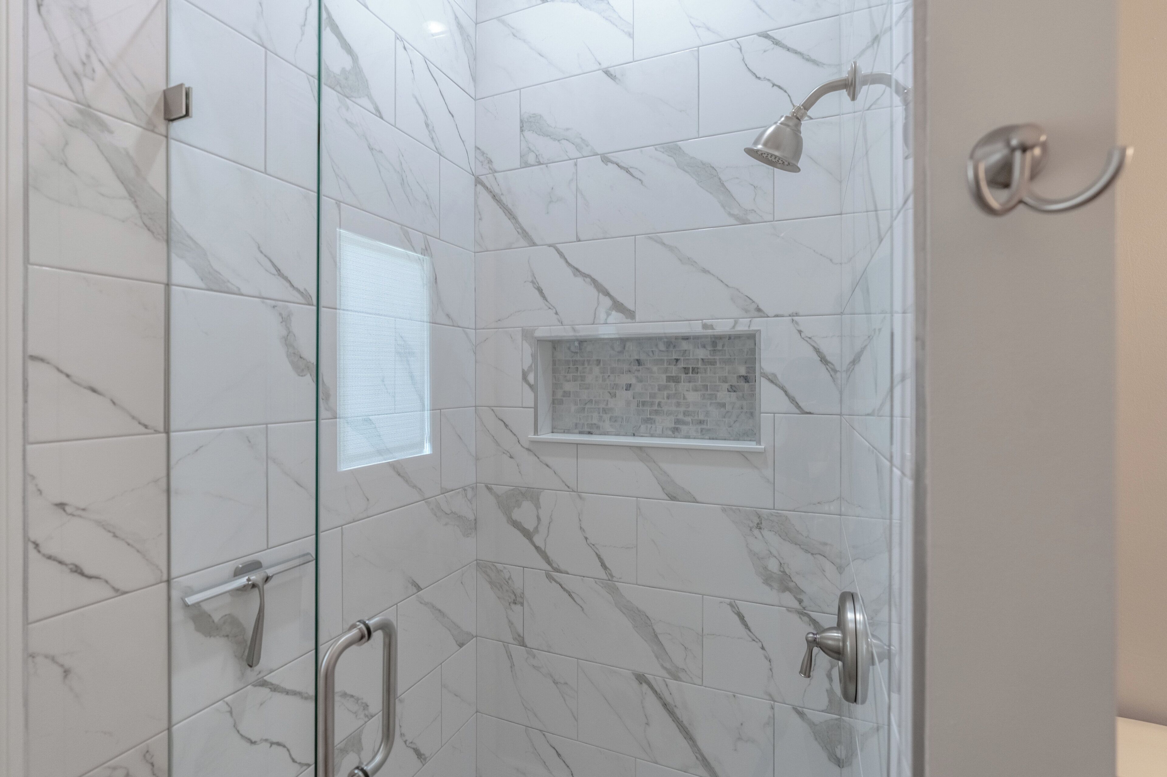 A walk-in shower with marble tiles, a glass partition, and a showerhead.