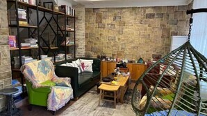 A cozy living room with a green armchair, a sofa, a wooden dining table, a hanging chair, and a bookshelf filled with books. - Qingfei Hostel (Yueqing)