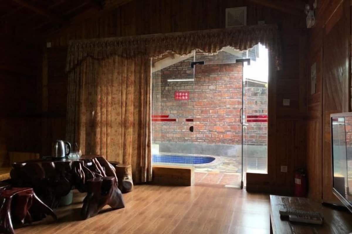 Un interior de madera con una pared de ladrillo, una puerta de cristal que da al exterior y una piscina visible a través de la puerta.
