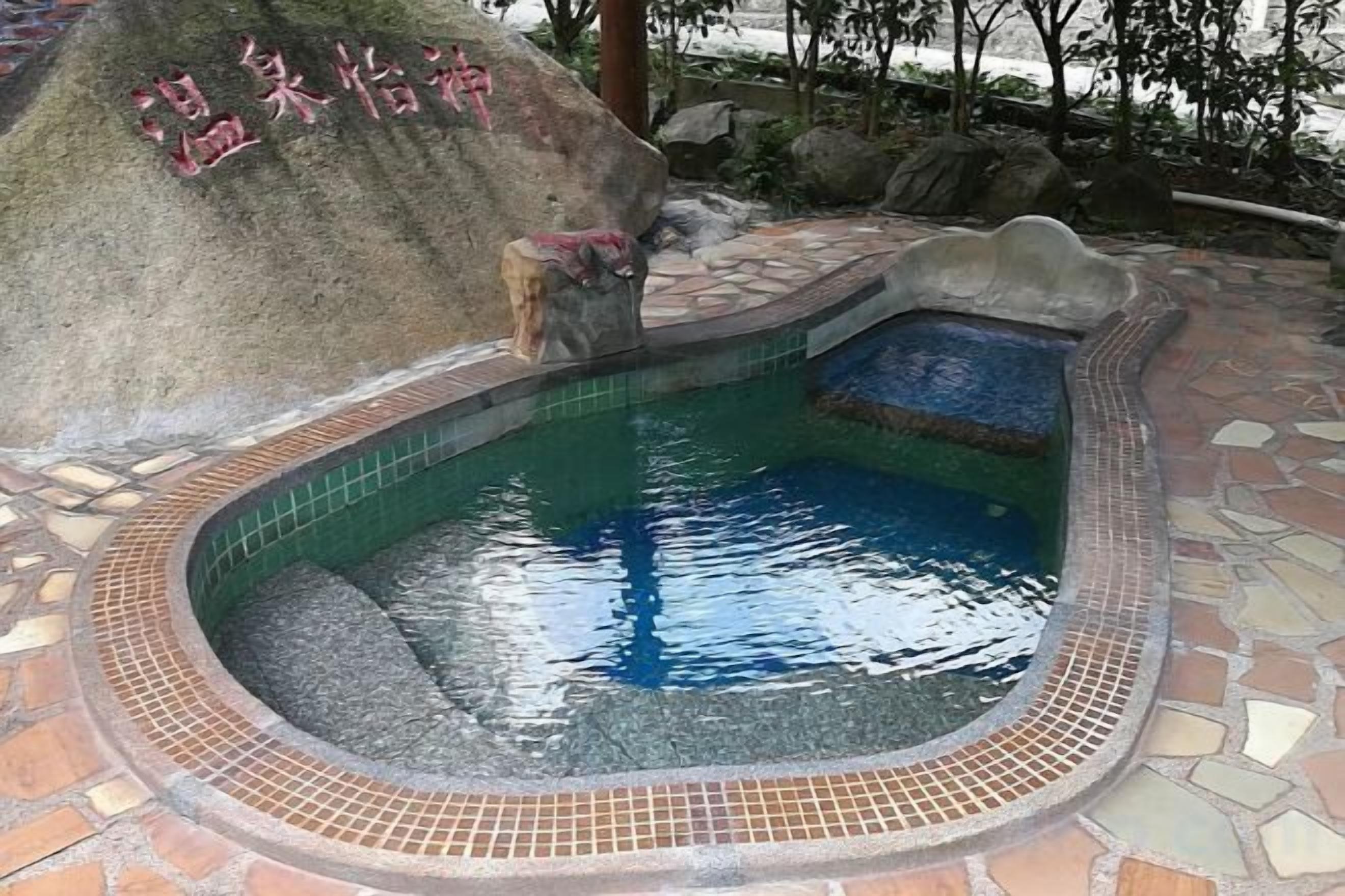 A hot spring area with a tiled pool, a stone bench, and a rock with Chinese characters.