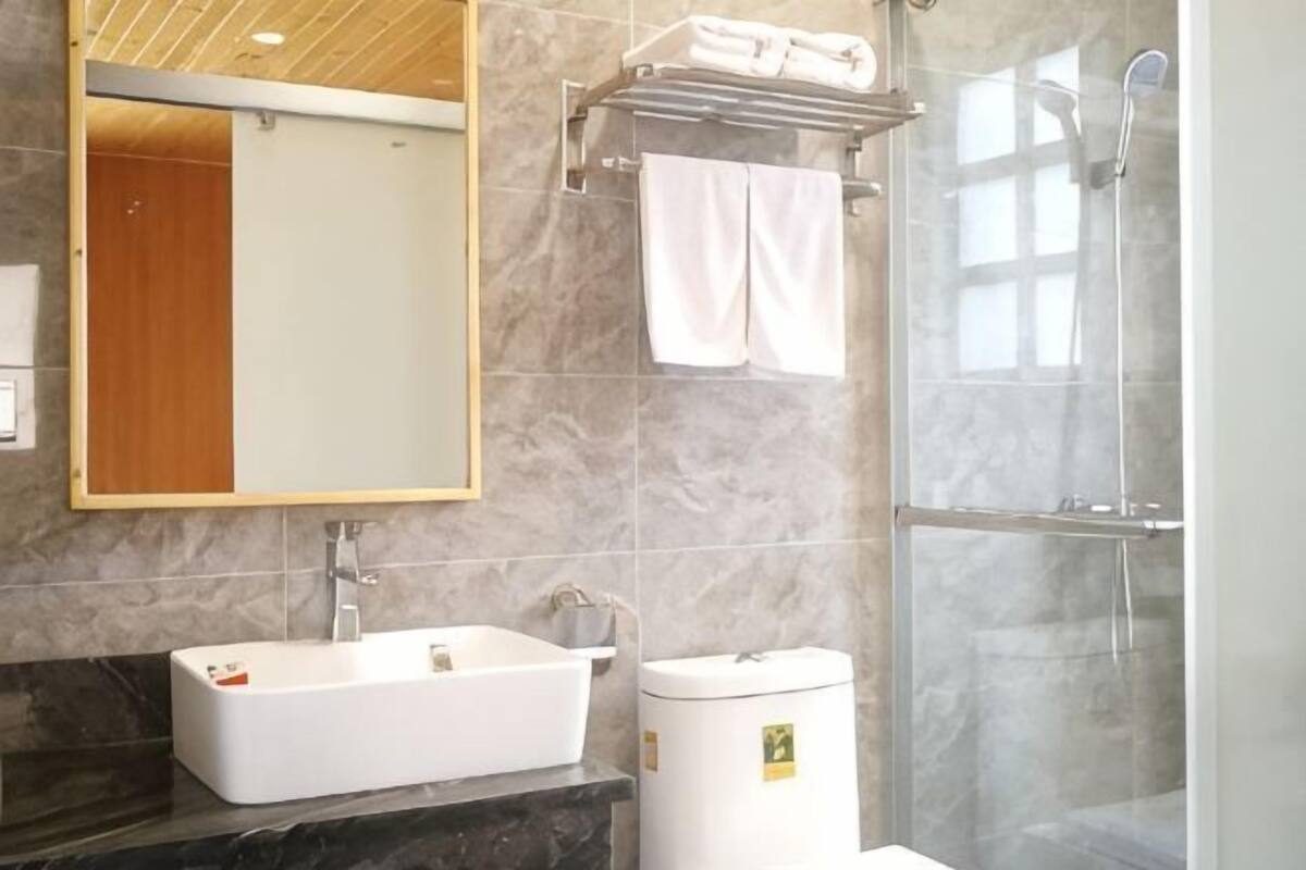 Un baño moderno con un lavamanos rectangular, un inodoro, una ducha con cerramiento de vidrio y un espejo con marco de madera.
