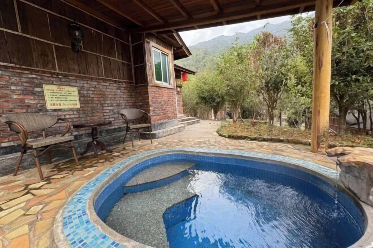 Un área de piscina con muro de ladrillo, terraza de madera y vistas a árboles y montañas.