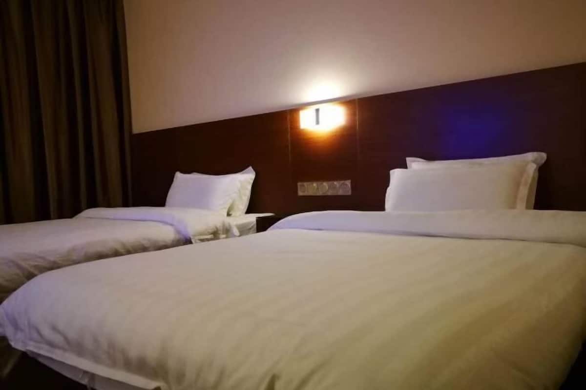 Habitación de hotel con dos camas, una lámpara fijada a la pared y un cabecero oscuro.