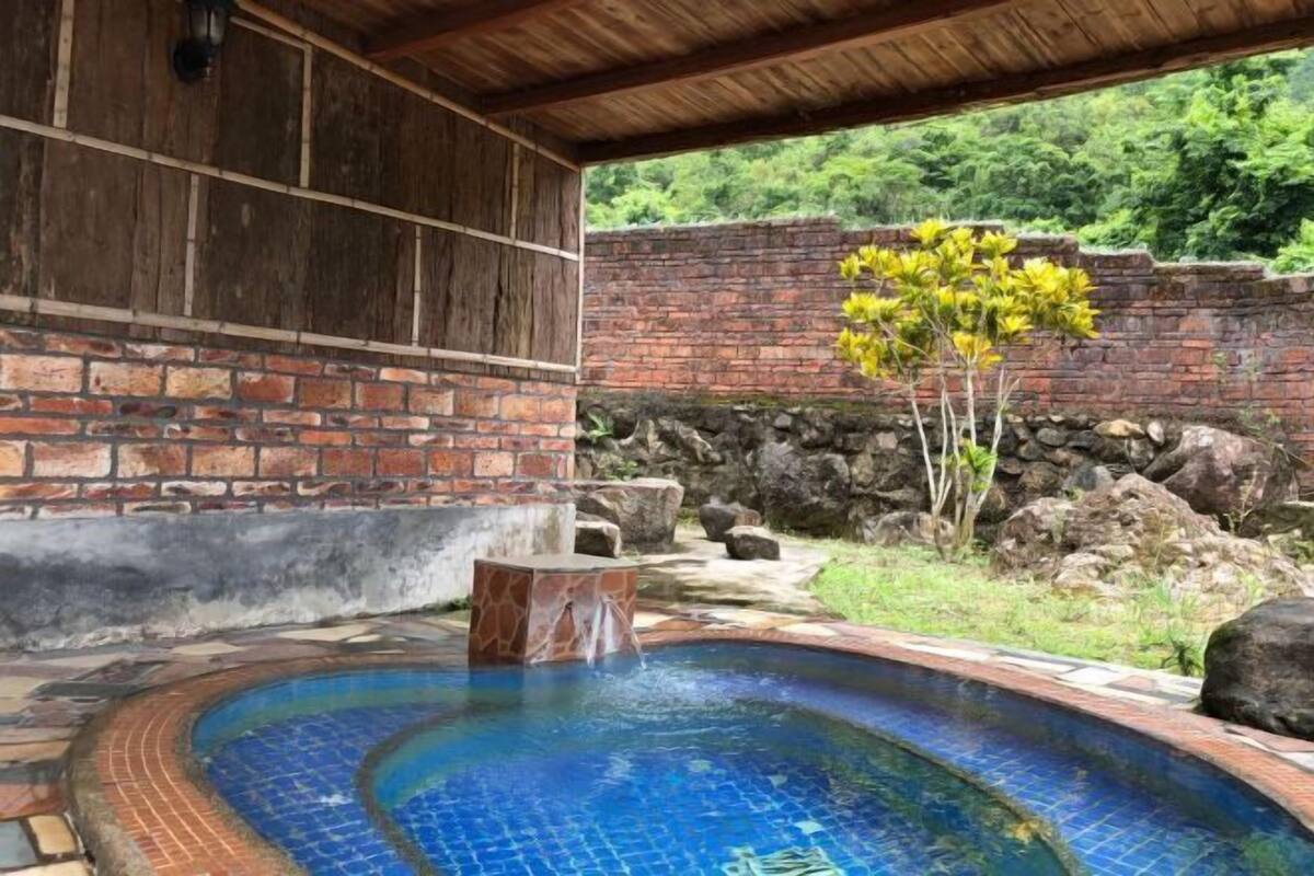 Un área de piscina con un muro de ladrillo, una pérgola de madera y una pequeña cascada.