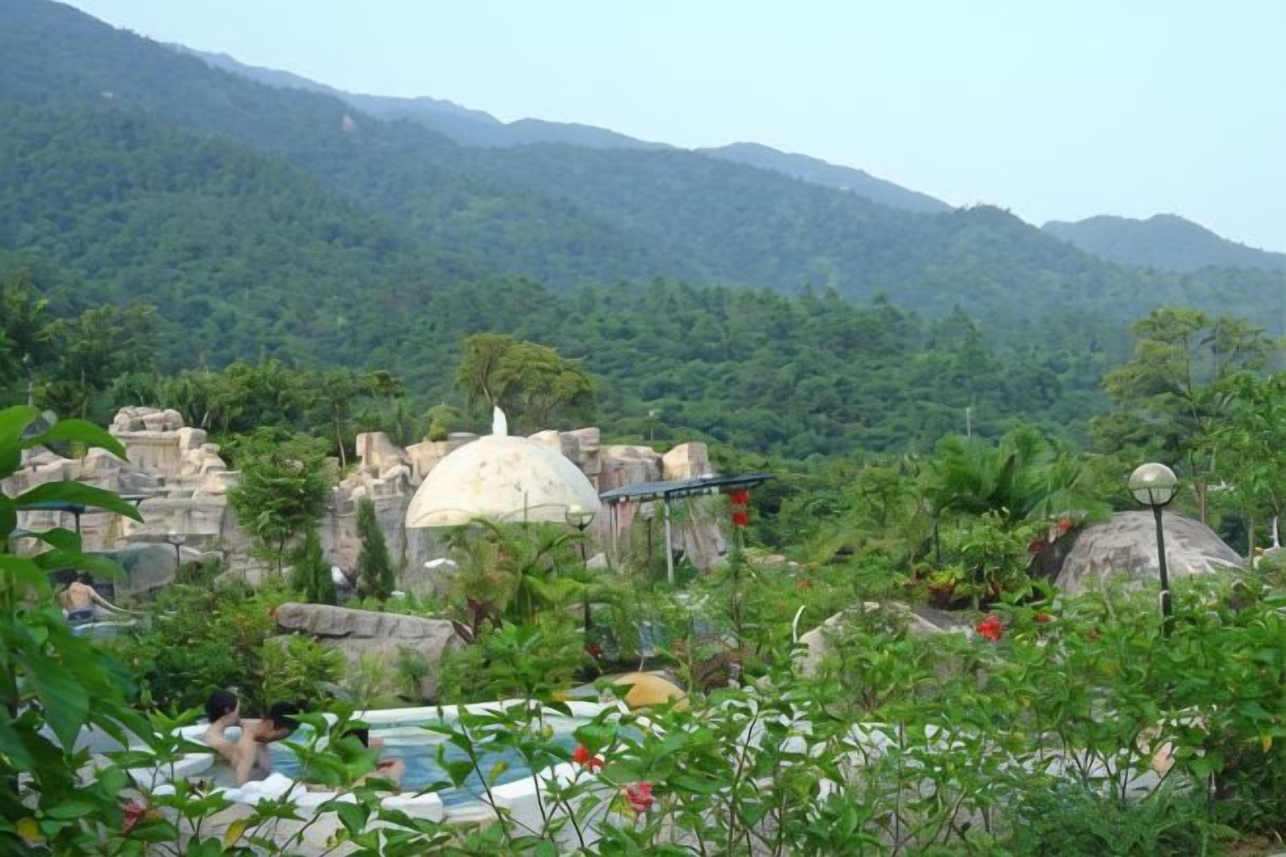 Un espace piscine doté d’une structure en forme de dôme, entouré d’une végétation luxuriante et avec des montagnes en arrière-plan.