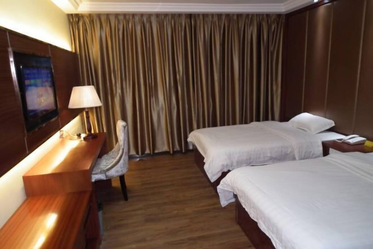 Una habitación de hotel con dos camas, un escritorio, una silla, un televisor y una cortina.