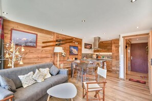 Uma sala de estar aconchegante com um sofá cinza, uma mesa pequena branca e uma área de jantar de madeira com cadeiras.