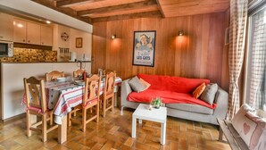 A cozy living area with a wooden ceiling, a dining table set with chairs, a sofa, and a small white table.