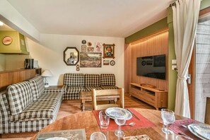 Un salon chaleureux avec un ensemble de canapés, un meuble TV en bois et une table à manger pour deux personnes.