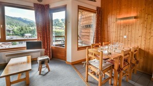 A cozy room with a wooden interior, a dining table set for four, and a view of a mountainous landscape through the windows.