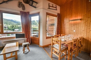 Um quarto aconchegante com decoração em madeira, uma mesa de jantar posta para quatro pessoas e vista para uma paisagem montanhosa pelas janelas.