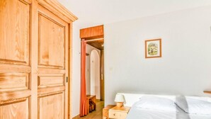 A bedroom with a bed, a nightstand, a wooden wardrobe, and a door leading to a bathroom. - Ski-in/ski-out & foot of the slopes, Ground floor, swimming pool, terrace, parking, 27m², Les Gets (Les Gets)