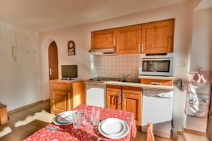 A compact kitchen with wooden cabinets, a microwave, a dishwasher, and a dining area set with a table and chairs.