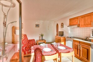 Un comedor acogedor con una mesa dispuesta para cuatro, armarios de madera, un televisor y una mesita auxiliar con un jarrón.