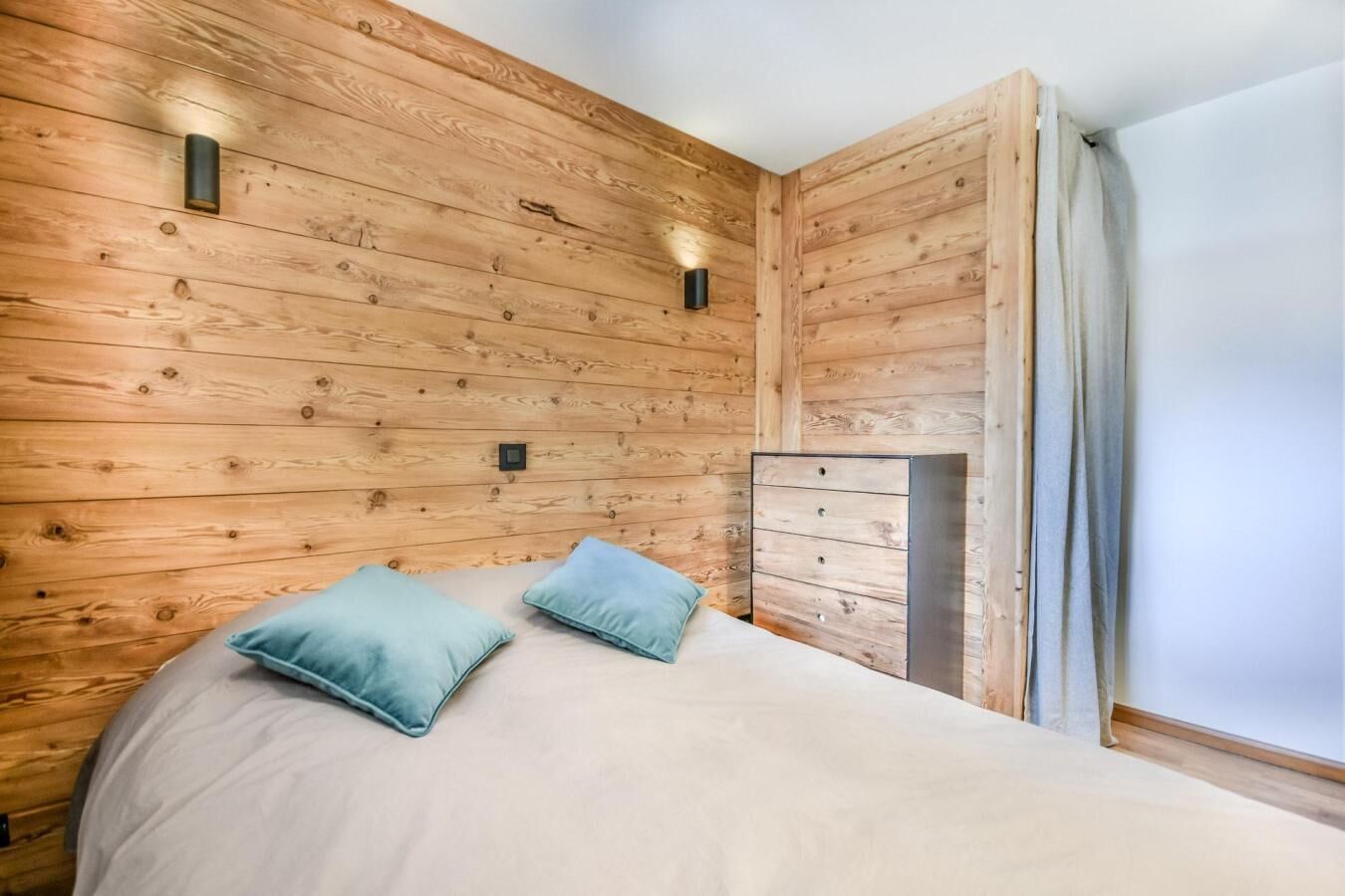 A bedroom with a wooden headboard, two pillows, a bed, a dresser, and a window with curtains.