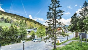 Un parking avec une voiture blanche, entouré d’arbres et d’un bâtiment doté d’un toit en pente.