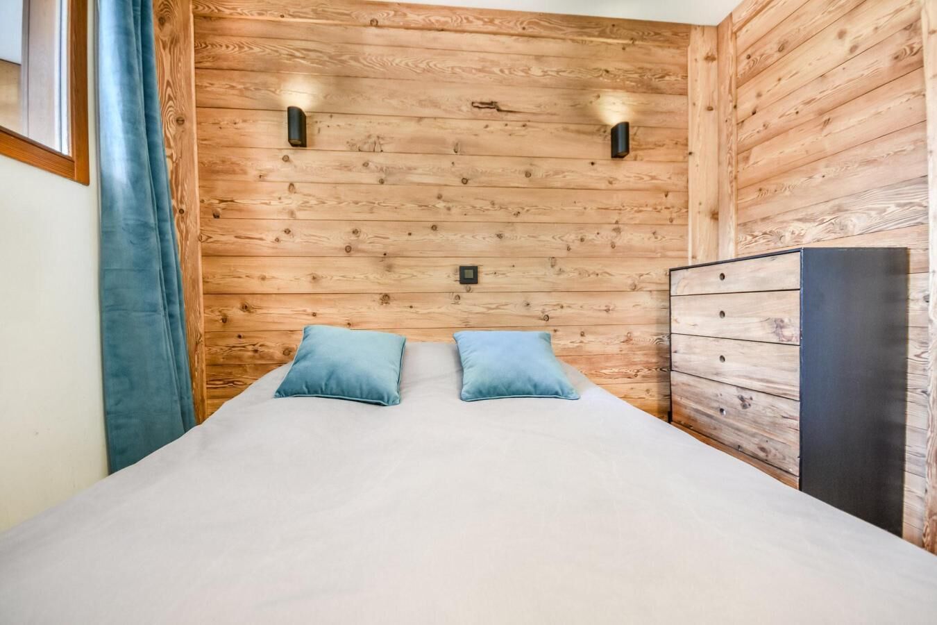 A room with a wooden slat wall, a bed with two pillows, and a dresser.
