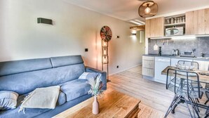 Un salon moderne avec un canapé bleu, une table basse en bois et un coin cuisine équipé d’un four à micro-ondes et de placards.