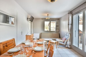 Een eetgedeelte met een houten tafel gedekt voor vier personen, een bank en een aan de muur bevestigde televisie.