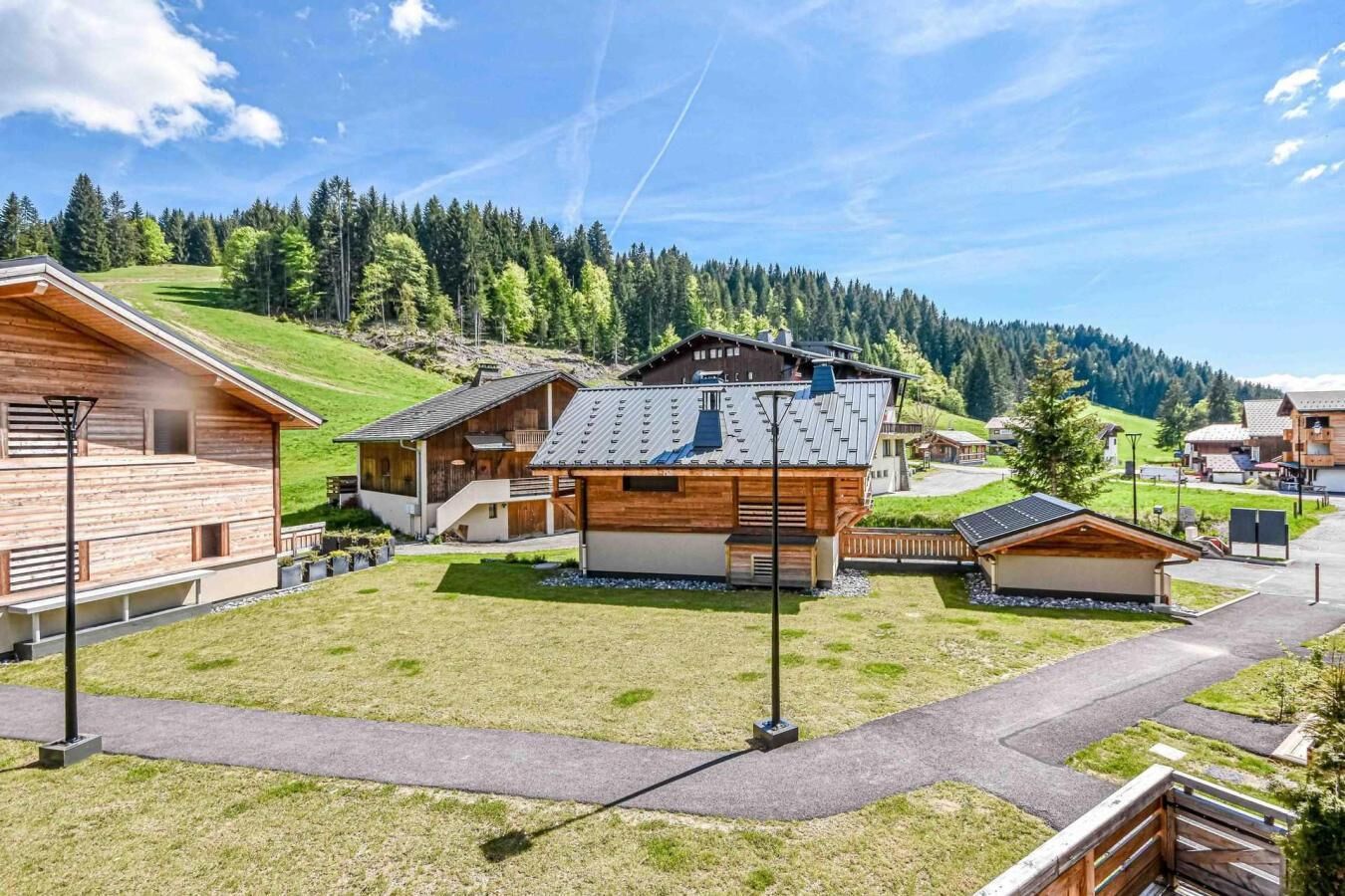 Un chalet moderne doté d’un bâtiment principal avec un toit en pente et une façade en bois, entouré de plus petits chalets et d’une pelouse bien entretenue.