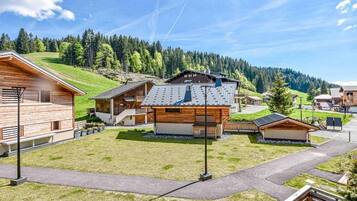 Un chalet moderne doté d’un bâtiment principal avec un toit en pente et une façade en bois, entouré de plus petits chalets et d’une pelouse bien entretenue.