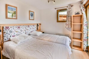 A bedroom with two beds, a wooden headboard, a window with curtains, and a shelf with patterned fabric. - Wifi, 1st floor, balcony, ski locker, 48m², Les Gets (Les Gets)