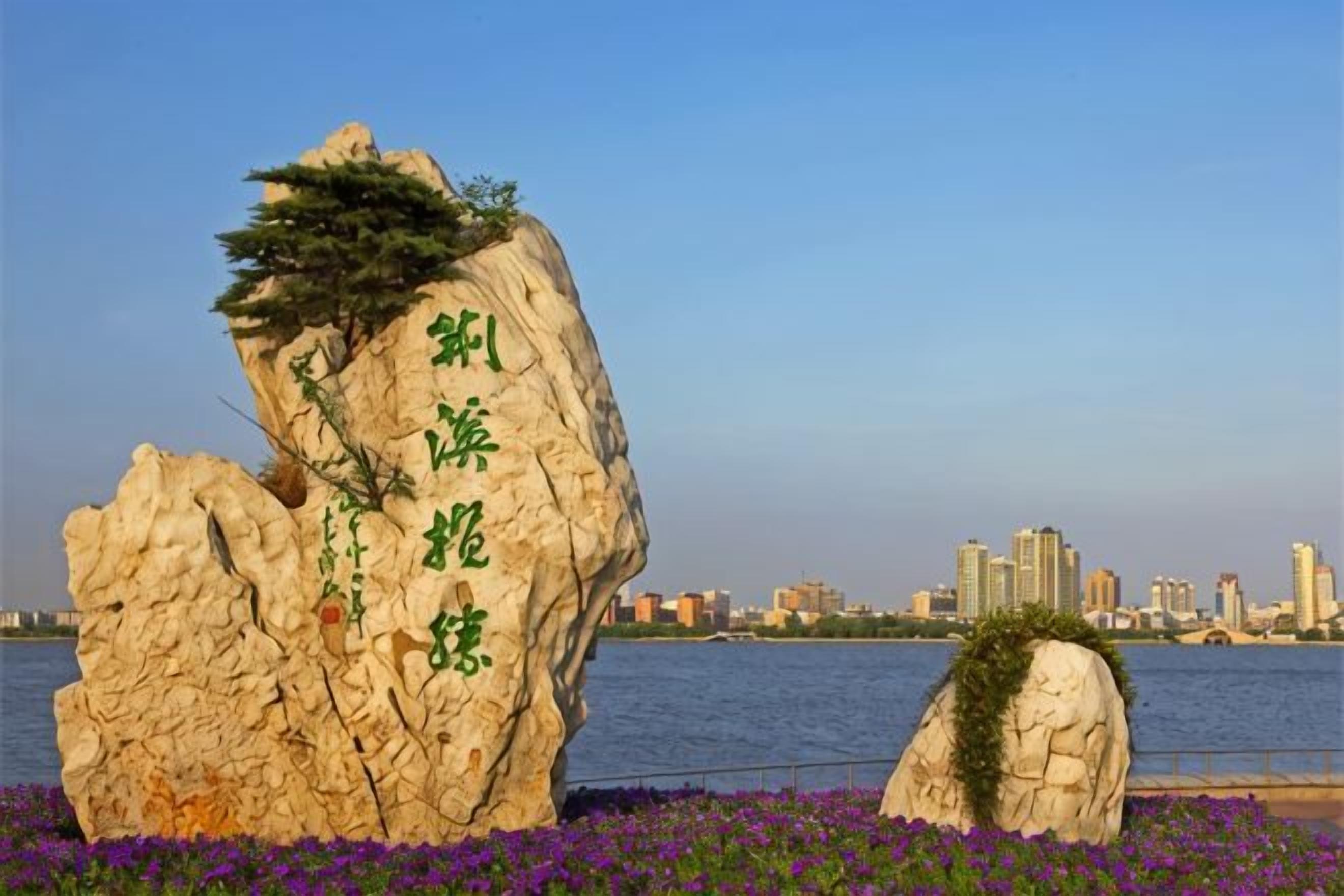 A rock formation with Chinese characters, a small tree, and purple flowers in the foreground.