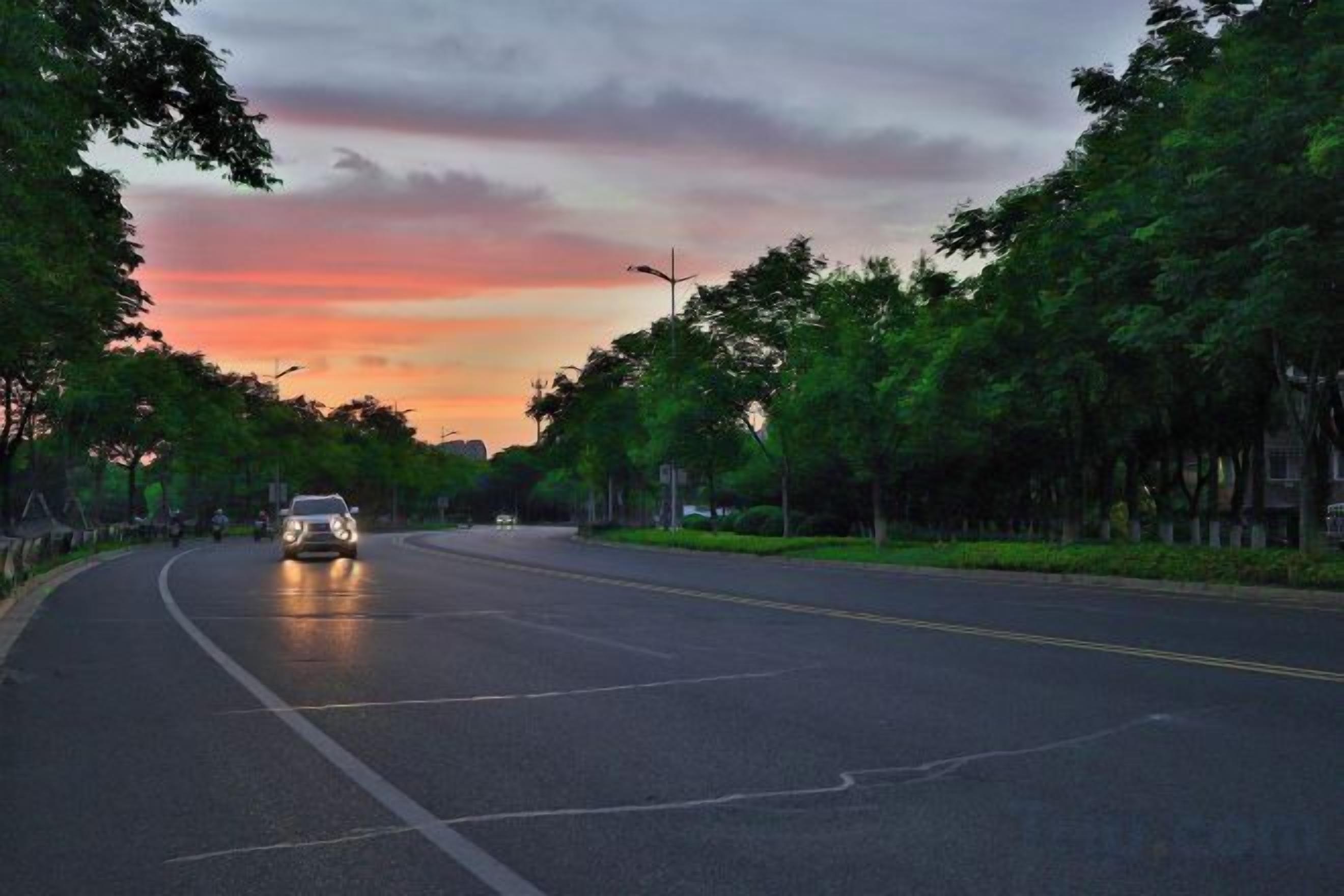 Una carretera con un vehículo, rodeada de árboles y un cielo al atardecer.
