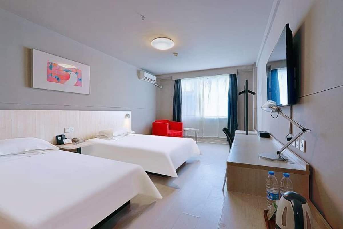 A hotel room with two beds, a desk with a lamp, a TV, and a painting on the wall.