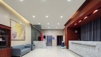 A modern hotel lobby with a reception desk, seating area, and a clock on the wall.