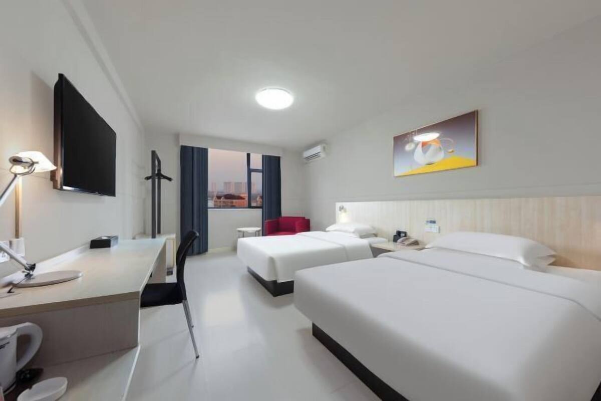 A hotel room with two beds, a desk with a chair, a TV, and a painting on the wall.