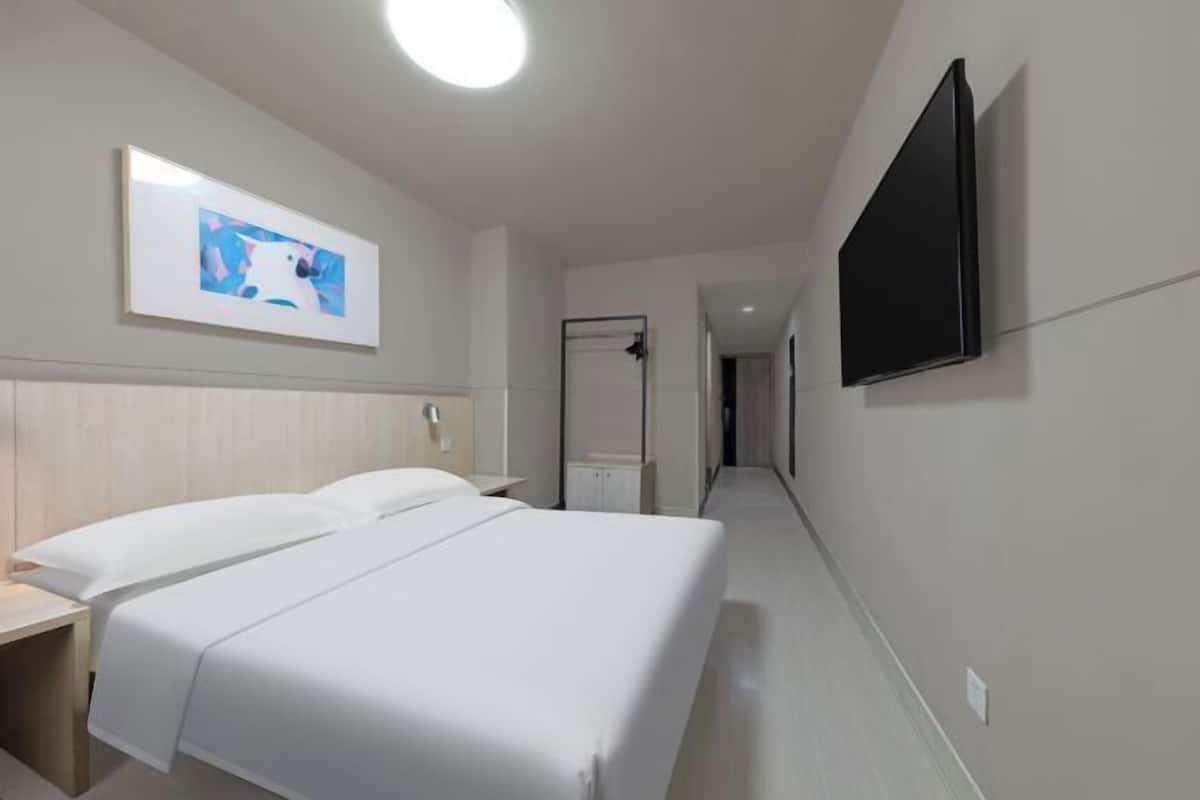 A hotel room with a bed, a bedside table, a TV mounted on the wall, and a framed picture above the bed.