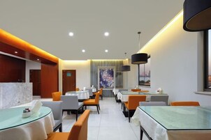 Comedor de hotel moderno con mesas redondas, sillas color naranja y vista de la ciudad a través del ventanal.