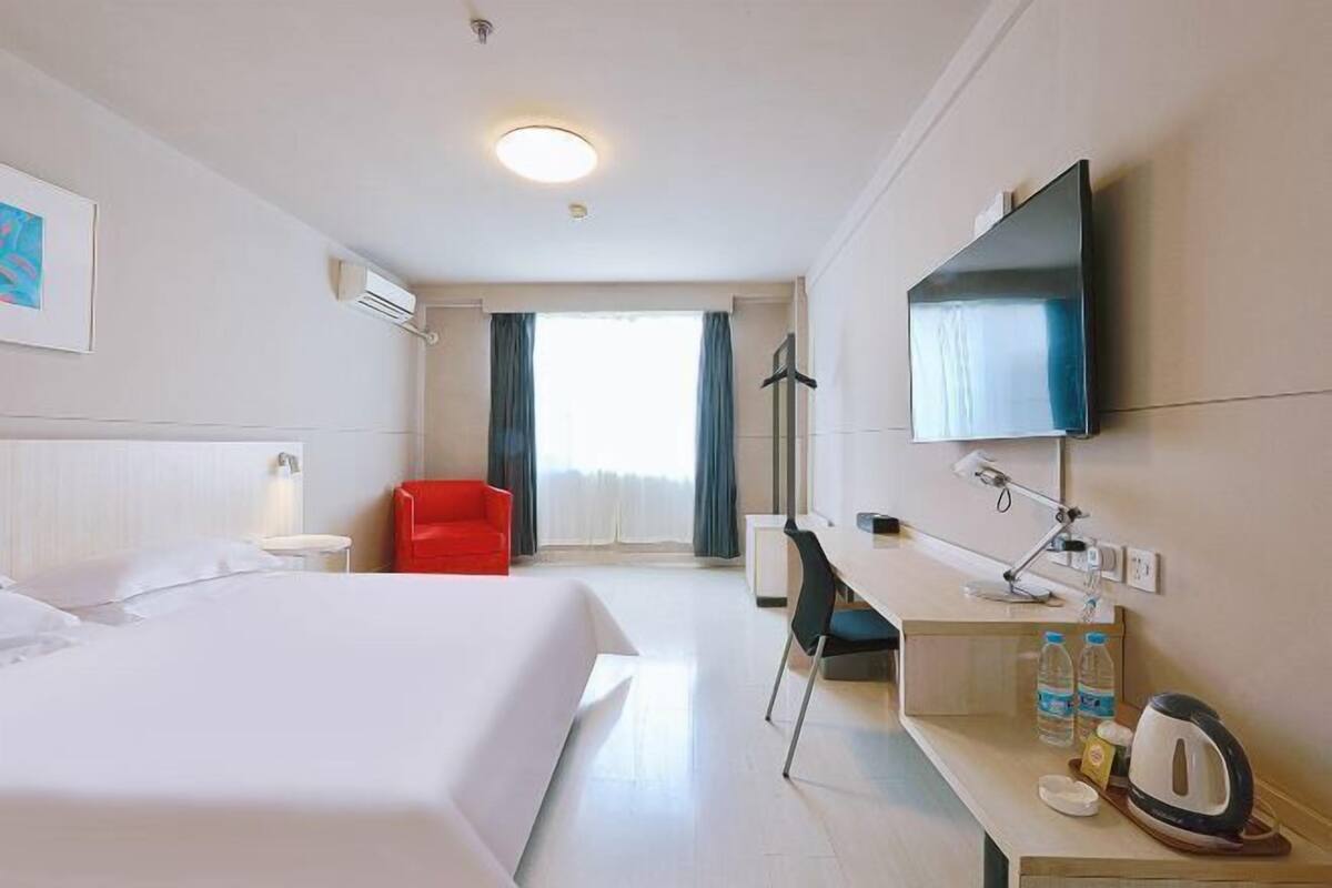 A hotel room with a bed, a desk, a chair, a TV, and a window with curtains.