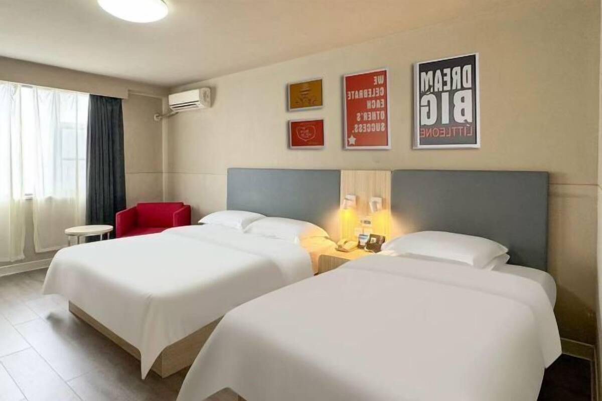 A hotel room with two beds, a red chair, a small table, and wall art.