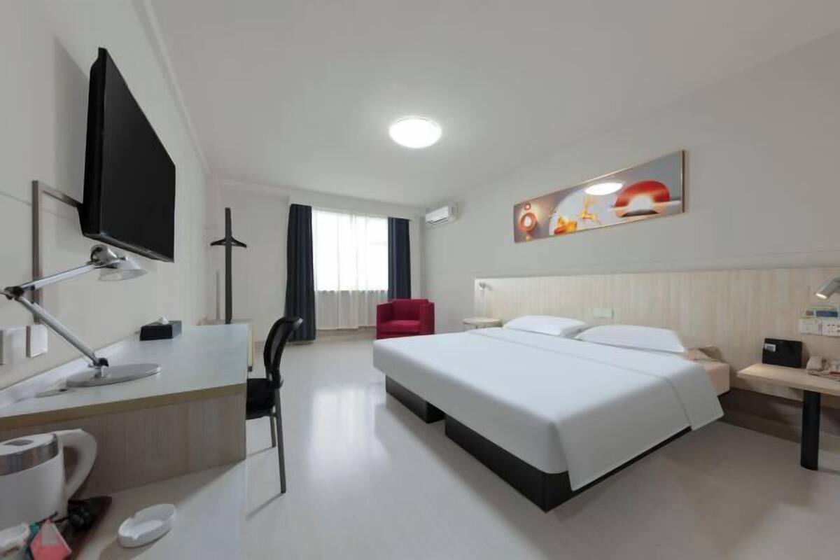 A hotel room with a bed, desk, chair, TV, and artwork on the wall.