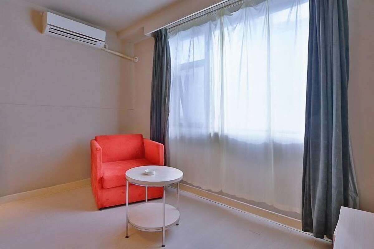 A room with a red sofa, a small round table, and a large window with sheer curtains.